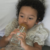 Toddler laying on a pillow with the Hevea Glass Wide Neck Bottle with natural rubber teat.