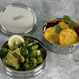 A close up of various food items inside 2 of the tins from the stainless steel A slice of green chapra two tier round lunchbox.