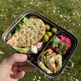 An adult hand holding the A slice of green large lunchbox with mini container outside and showing various foot items inside the main compartment and mini container