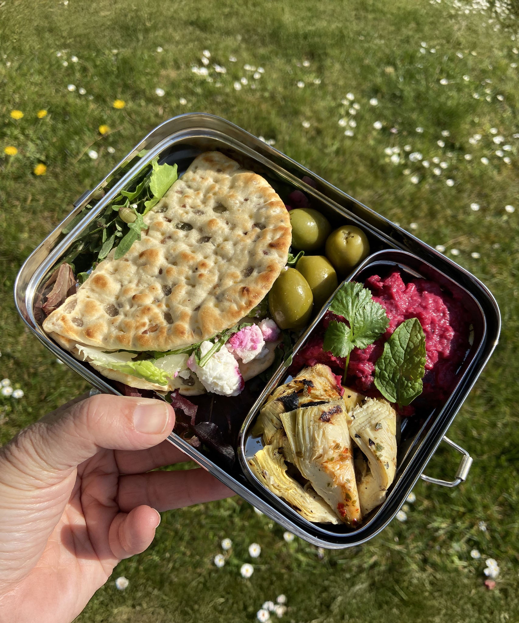 An adult hand holding the A slice of green large lunchbox with mini container outside and showing various foot items inside the main compartment and mini container