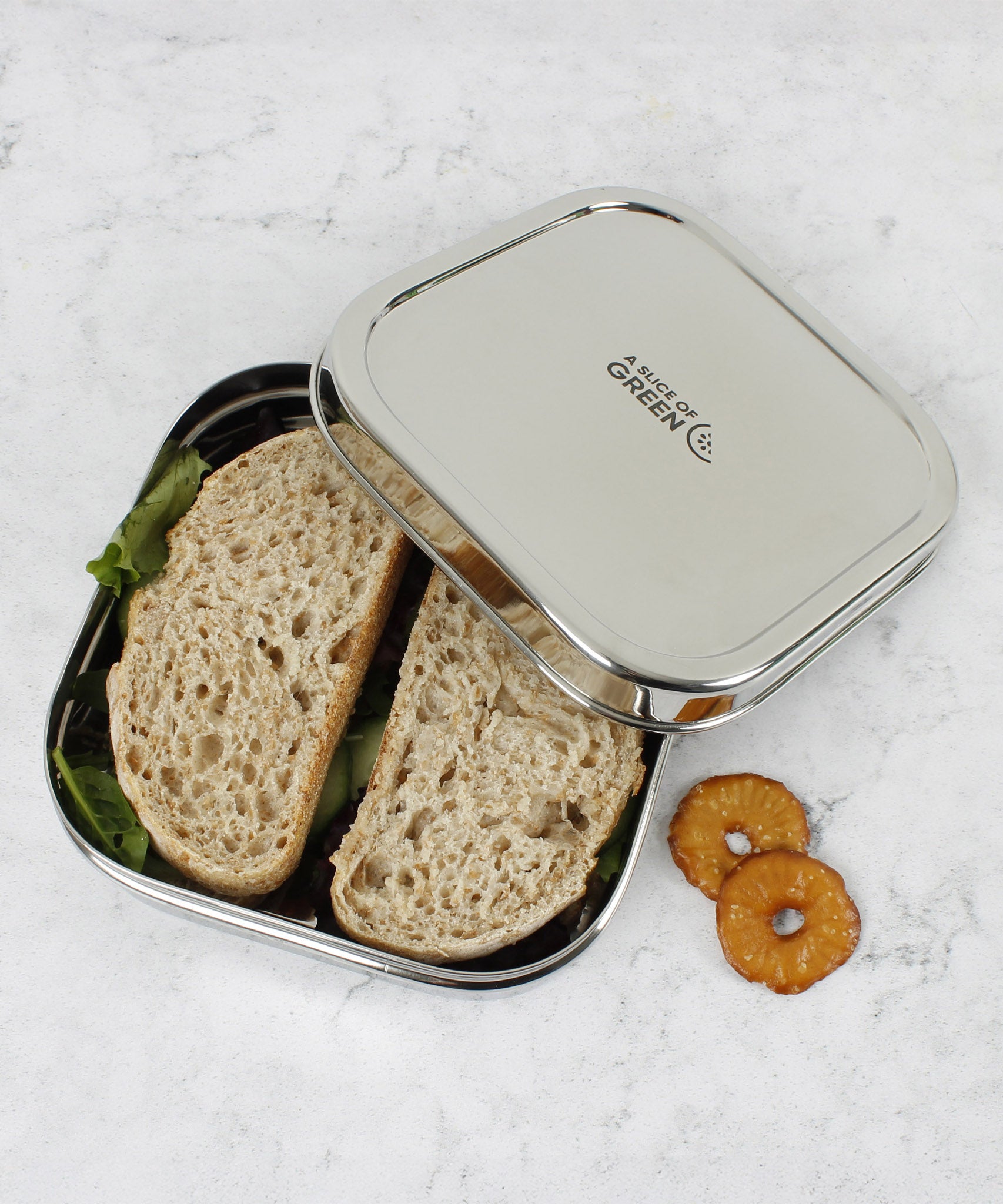 A top down image of A slice of green shimla large square container lunchbox with the lid resting on top showing the stainless steel finish detail