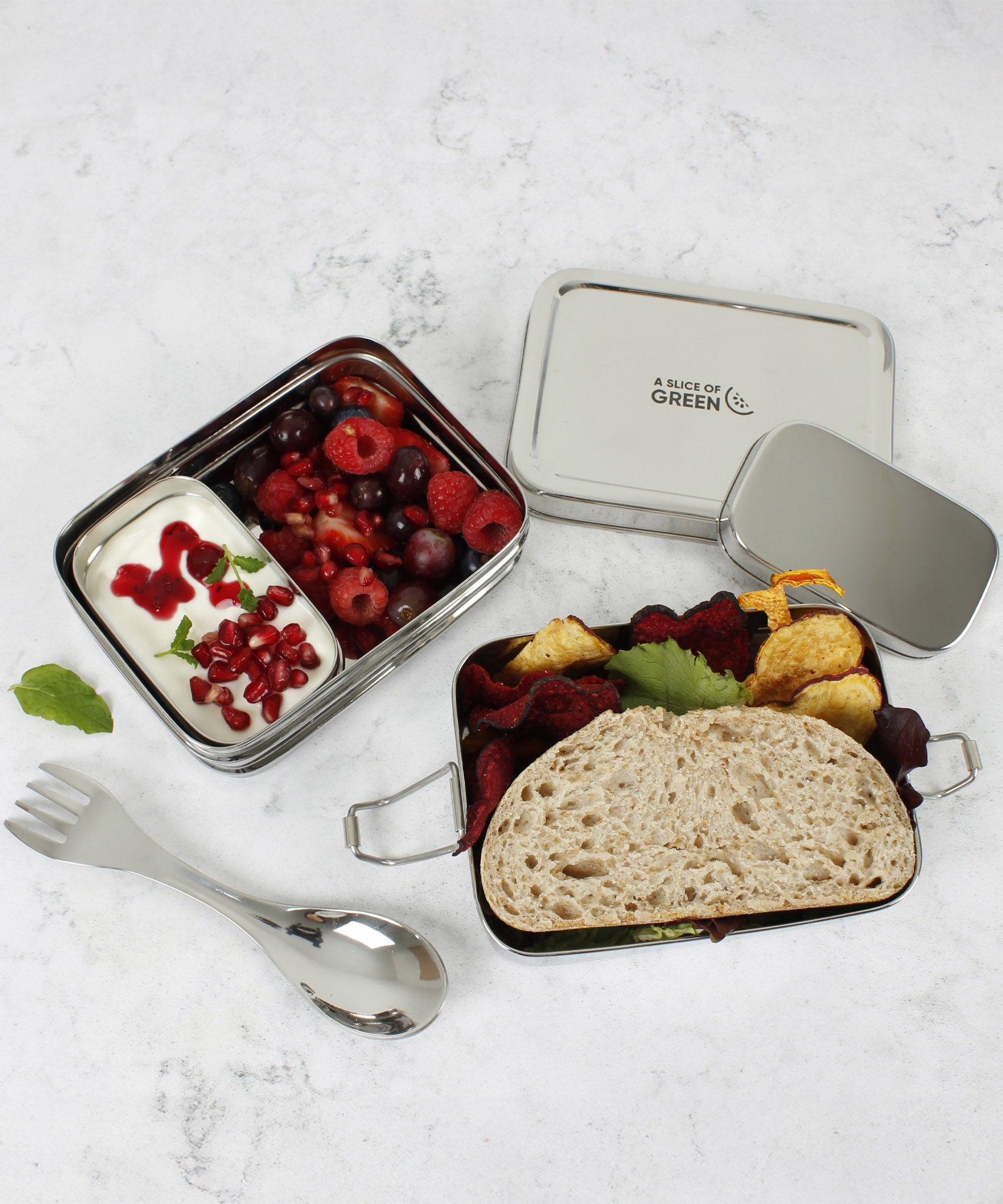 A top down image of A slice of green two tier lunchbox with mini container showing various food and fruit items inside each compartment