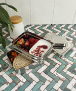 A slice of green two tier lunchbox with mini container resting on a kitchen counter