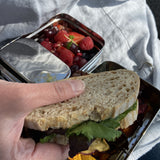 A close up of an adult holding a sandwich above the A slice of green two tier lunchbox with mini container