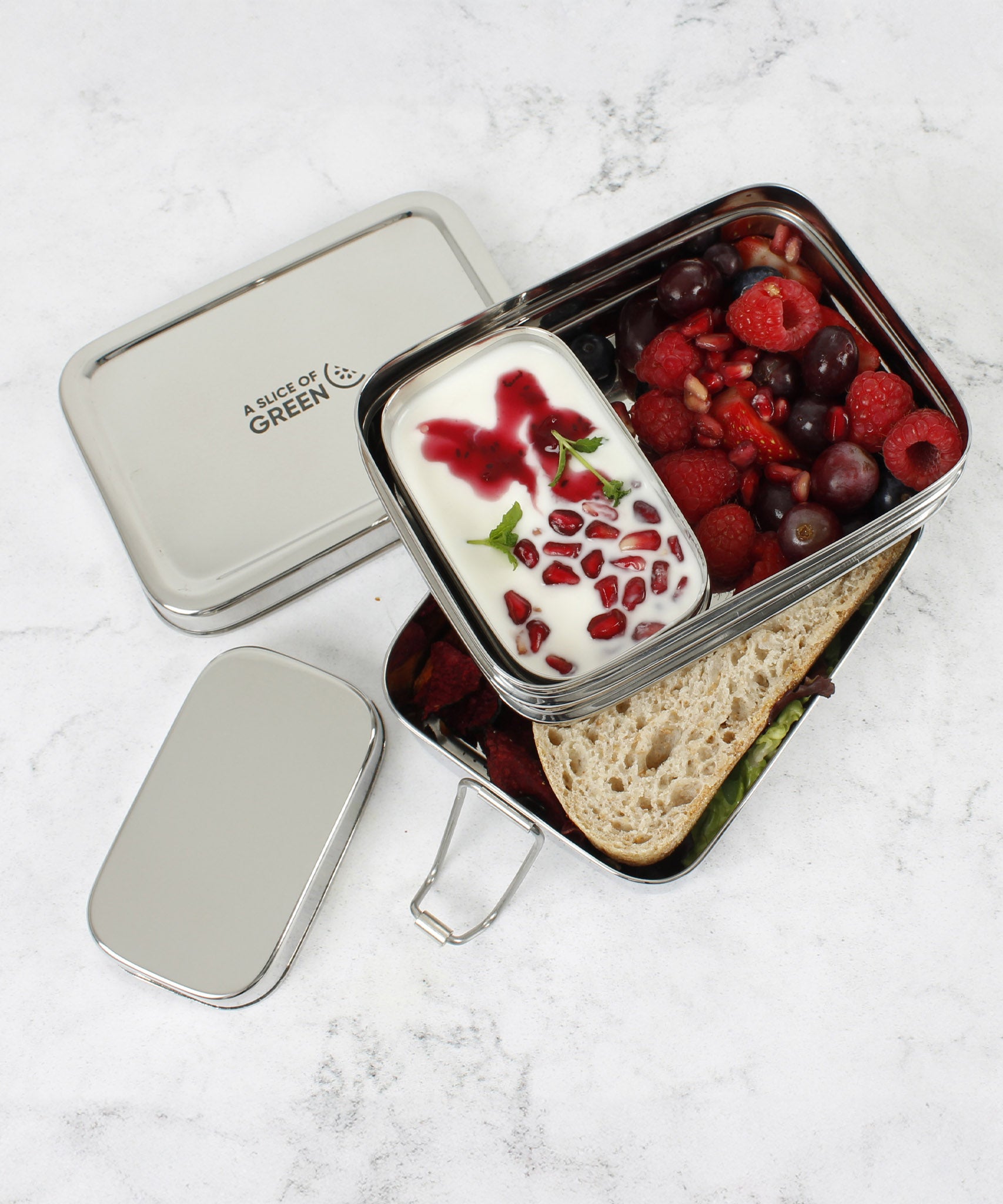 A top down image of A slice of green two tier lunchbox with mini container stacked on top of eachother and showing various ruit items inside each compartment