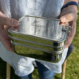 A close up of an adult holding the A slice of green two tier lunchbox with mini container