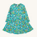 The Frugi Sofia skater dress with a wild woods print design on a green background. The print features flowers and toadstools.