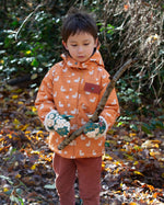 Boy playing in a forest, wearing a hooded Little Green Radicals Waterproof Winter School Coat, made from recycled bottles, with a yellow gold duck print, for sale at Babipur.