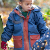 Girl in a forest wearing a hooded Little Green Radicals Waterproof Winter School Coat, made from recycled bottles, PFC Free, with a Moonlight Blue print with deep red details down the zip and front pockets, for sale at Babipur.