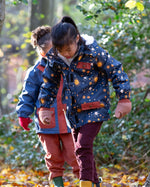 Child playing in a forest wearing a Kids Warm Waterproof Winter School Coat in a navy night moon print, blue and floral, by Little Green Radicals, made from recycled bottles and a cosy polyester fleece, buy now at Babipur.