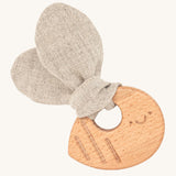 The Hempions Bee Baby Teether is an adorable baby teething toy made from natural hemp textile and solid wood, in the shape of a bee. The image shows the wooden textured bee teething ring with a light grey/beige hemp bee wing shaped fabric attached to it, on a cream background