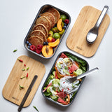 A top down view showing the different cutlery from the Black + Blum stainless steel cutlery set on top of food inside the original lunchboxes.