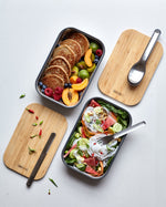 A top down view showing the different cutlery from the Black + Blum stainless steel cutlery set on top of food inside the original lunchboxes.