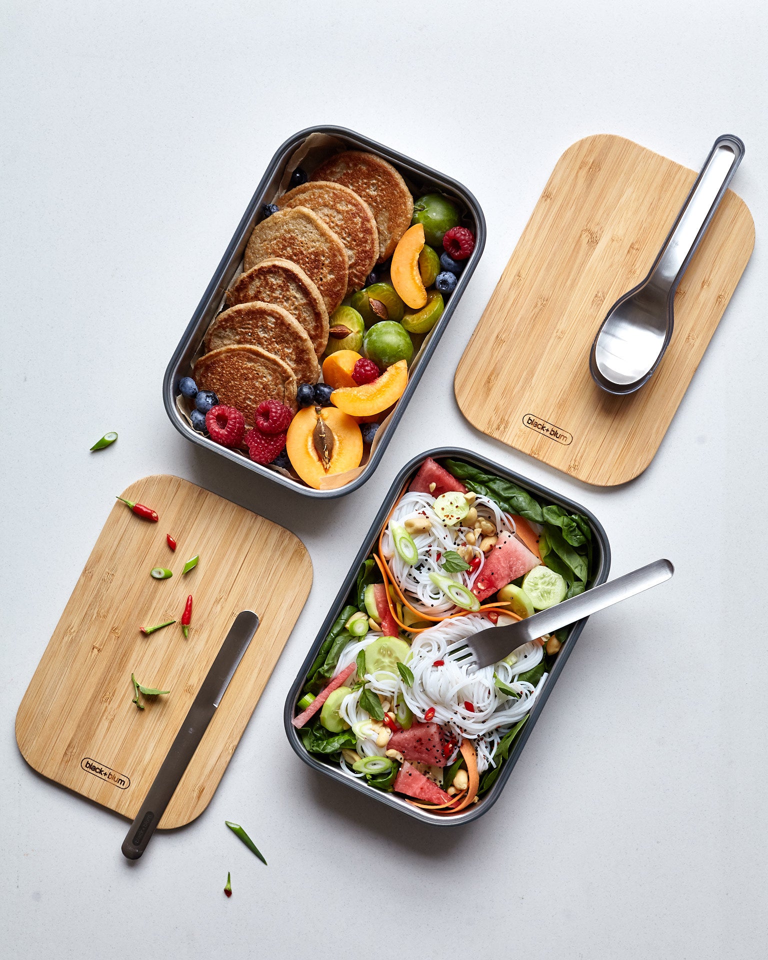 A top down view showing the different cutlery from the Black + Blum stainless steel cutlery set on top of food inside the original lunchboxes.