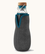 Black + Blum glass bottle with active charcoal water filter and locking coil available at Babipur. Features a felted holder with dark blue trim and a cork lid with a loop handle