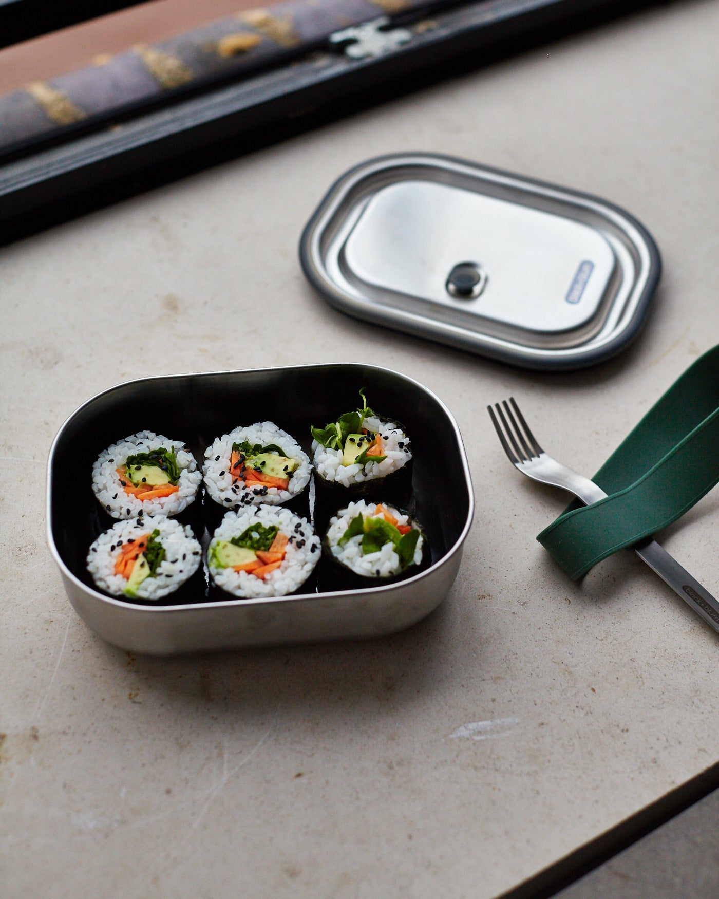 A close up of the Black + Blum leakproof stainless steel lunchbox with a olive silicone showing the size of the box with food inside