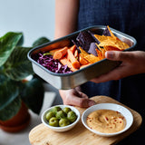 A close up of a adult holding the Black + Blum stainless steel airtight stainless steel sandwich box with the bamboo lid used as a serving plate