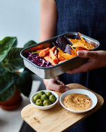 A close up of a adult holding the Black + Blum stainless steel airtight stainless steel sandwich box with the bamboo lid used as a serving plate