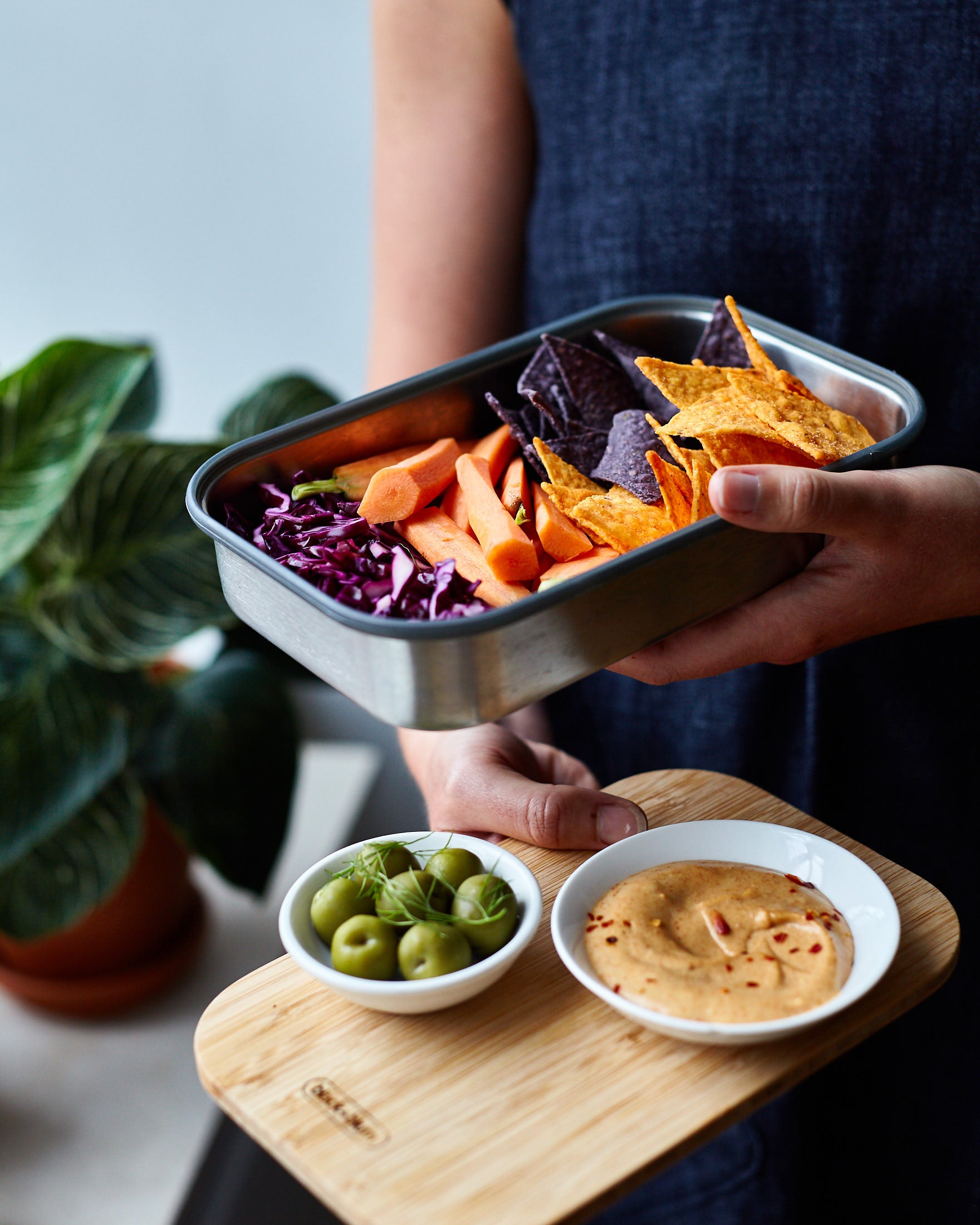 A close up of a adult holding the Black + Blum stainless steel airtight stainless steel sandwich box with the bamboo lid used as a serving plate