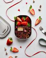 A top down view of the Black + Blum leakproof stainless steel lunchbox with a olive silicone holder on top of red decorative ribbon with a chocolatey desert inside the lunchbox