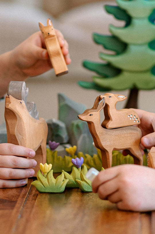 Bumbu Wooden animal toys on a table with children's hands interacting with them.