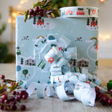 A box on a table wrapped in Babipur Christmas paper. There's a roll of babipur Christmas paper tape on top of the box.