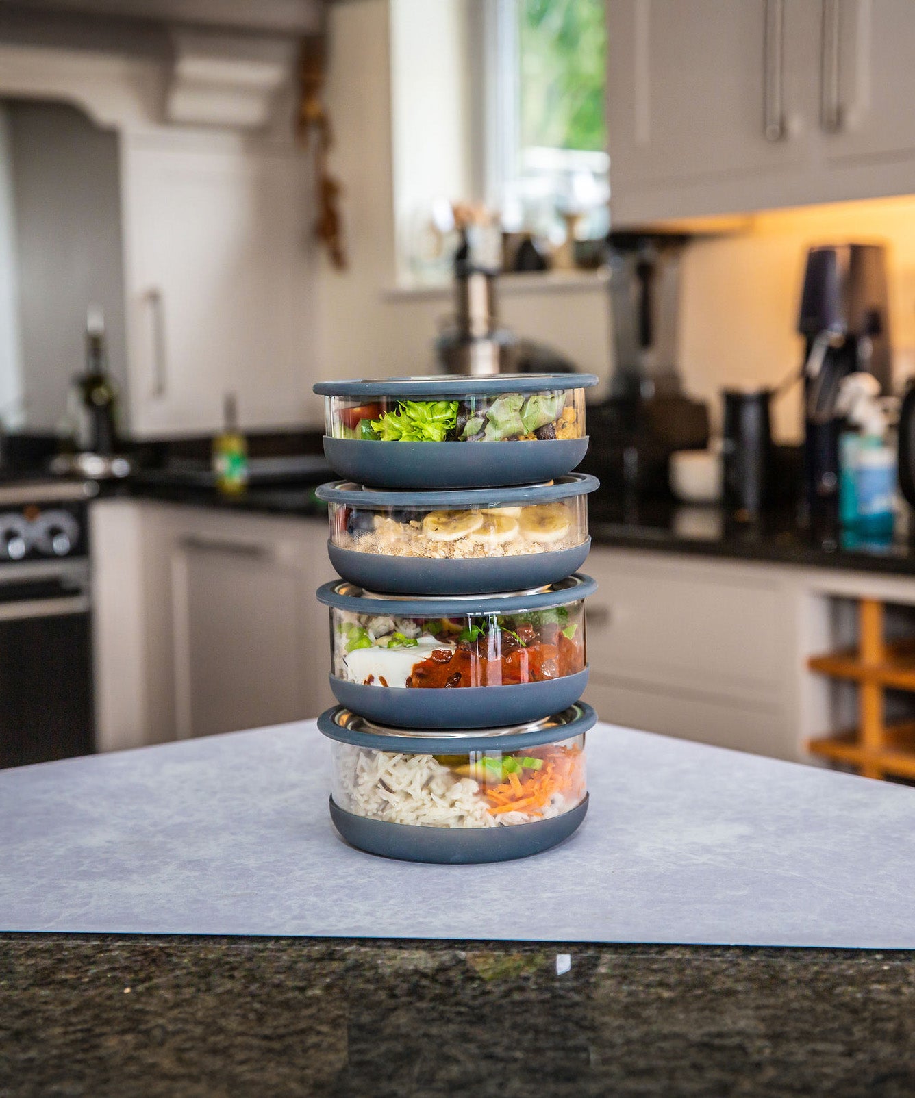 A stack of medium and large Elephant box lunch bowls on a kitchen counter and packed with different foods. Both bowls are available at Babipur.