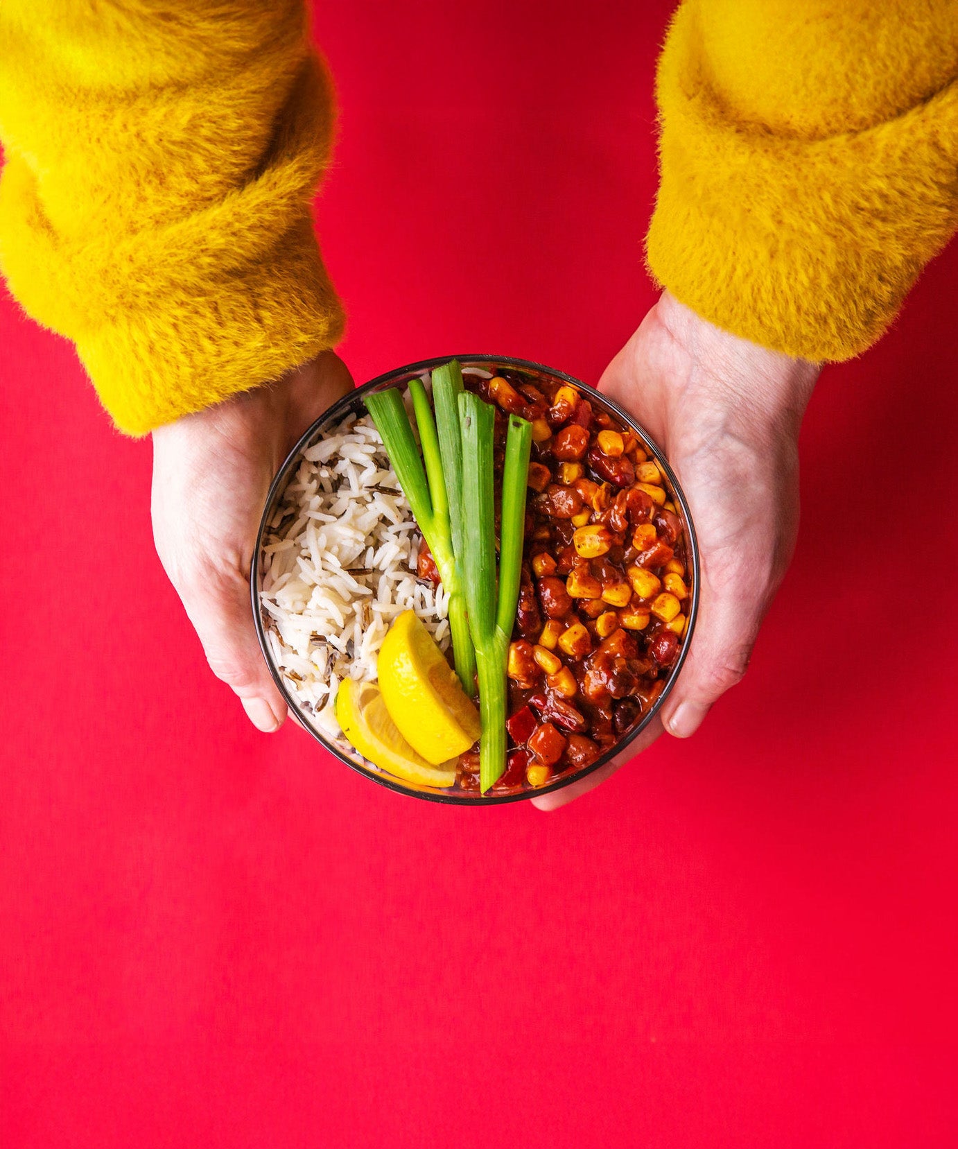 An adult hand holding the Elephant box large lunch bowl full of food and against a bright red background. Lunch bowl available at Babipur.