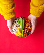 An adult hand holding the Elephant box large lunch bowl full of food and against a bright red background. Lunch bowl available at Babipur.