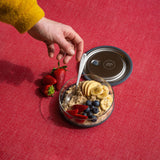 An adult hand reaching out for a spoon in the Elephant box medium lunchbowl full of different fruit. Lunch bowl available at Babipur