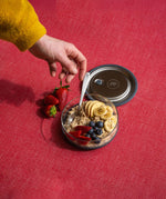 An adult hand reaching out for a spoon in the Elephant box medium lunchbowl full of different fruit. Lunch bowl available at Babipur