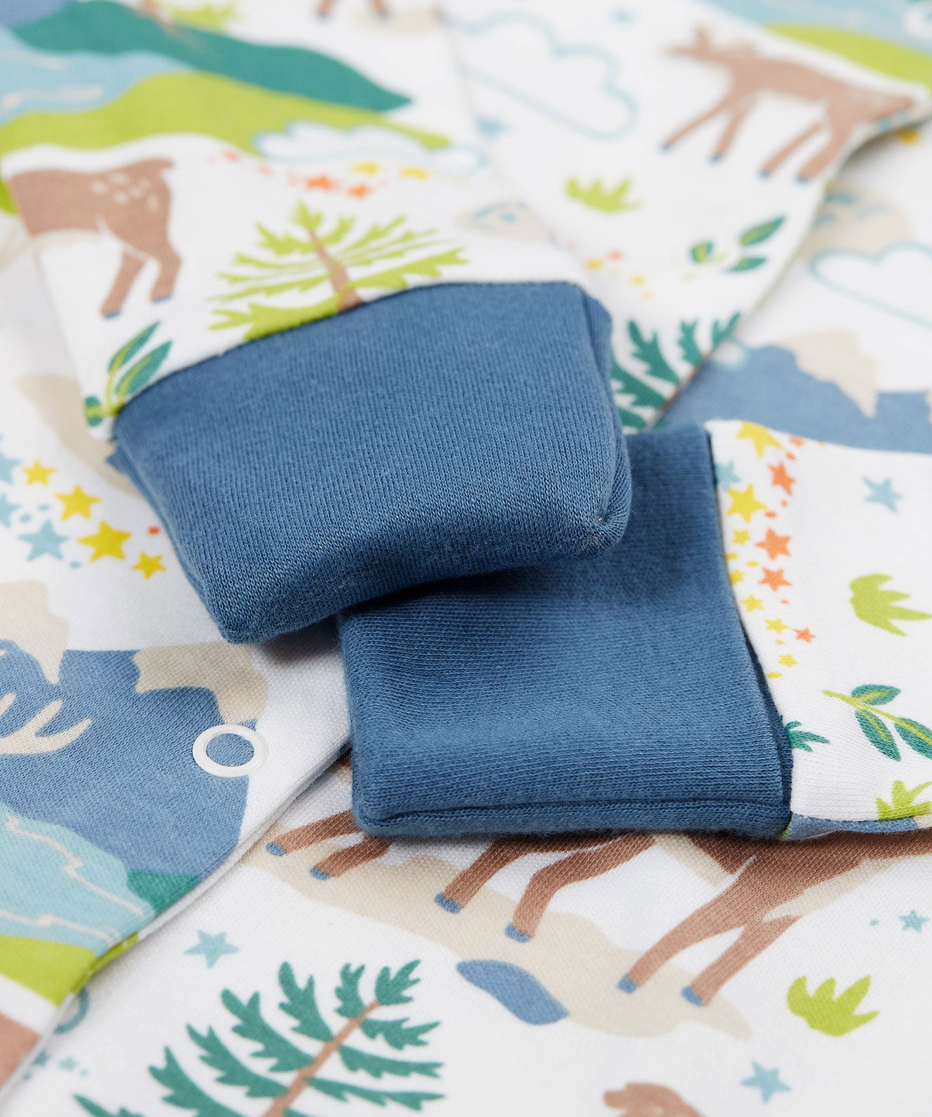 A close up of the navy coloured cuffs that can fold over in place of scratch mitts on the A Frugi Caribou Fields Organic Cotton Lovely Babygrow. A white babygrow with a reindeer themed print with green and blue details. This babygrow is a part of a wide range of organic cotton clothing for children available here at Babipur.