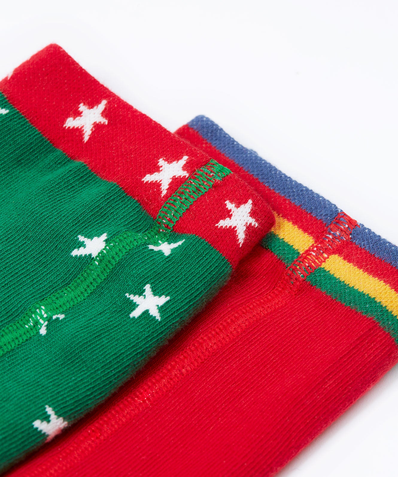 A close up of the waistbands on the Frugi Norah tights in green robin and berry red 2 pack available at Babipur. A pair of GOTS organic cotton tights in green with white stars and a robin design. Other pair is a bright festive red.