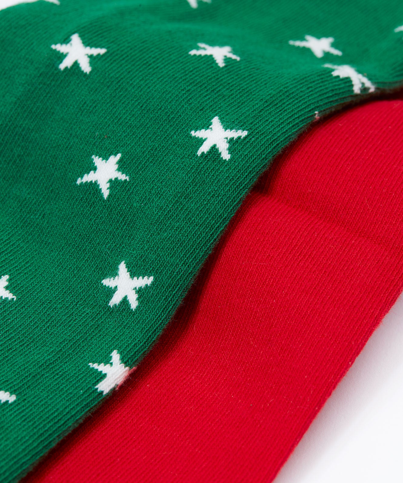 A close up of the material on the Frugi Norah tights in green robin and berry red 2 pack available at Babipur. A pair of GOTS organic cotton tights in green with white stars and a robin design. Other pair is a bright festive red.