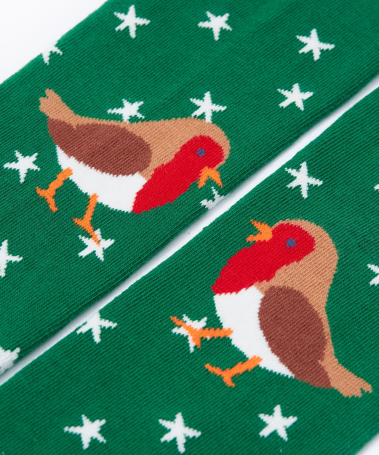 A close up of the robin details on the green pair of norah tights from the. Frugi Norah tights in green robin and berry red 2 pack available at Babipur. A pair of GOTS organic cotton tights in green with white stars and a robin design. Other pair is a bright festive red.