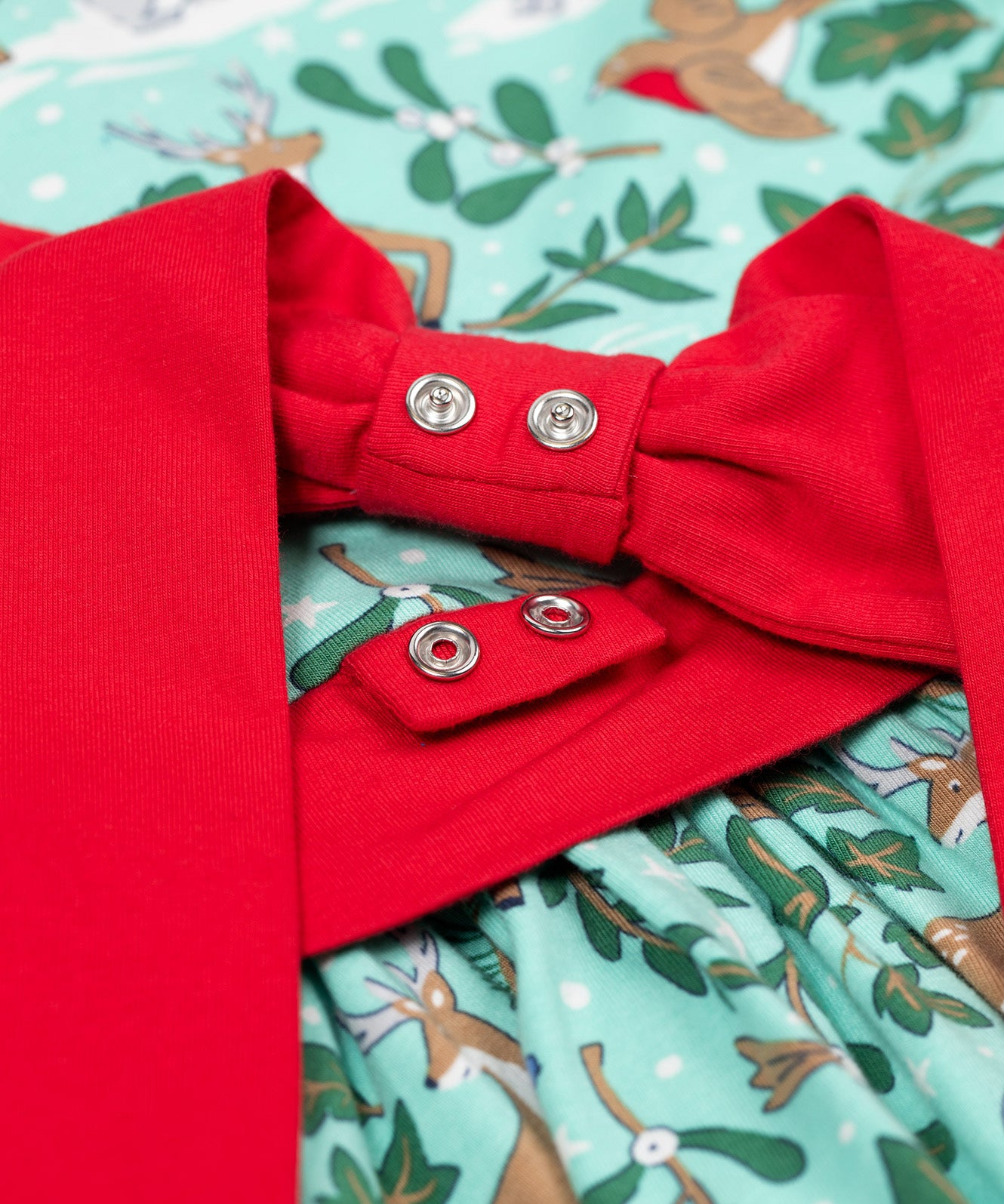 A close up of the red bow that can be poppered onto the back of the Frugi party skater dress in festive forest available at Babipur. A GOTS organic cotton dress in mint green with a playful winter / festive print. Features a red tie around the waist