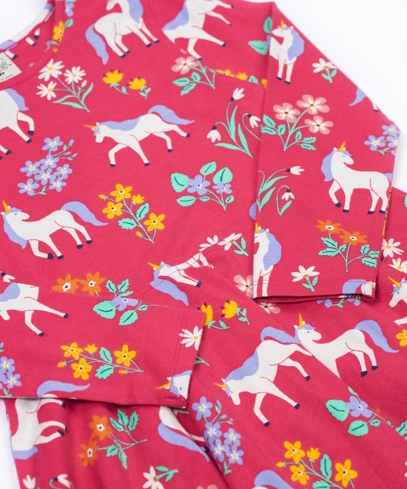 A close up of the Frugi sofia skater dress in rose / unicorn floral available at Babipur. A GOTS organic cotton dress in light pink with a cute unicorn and floral design.