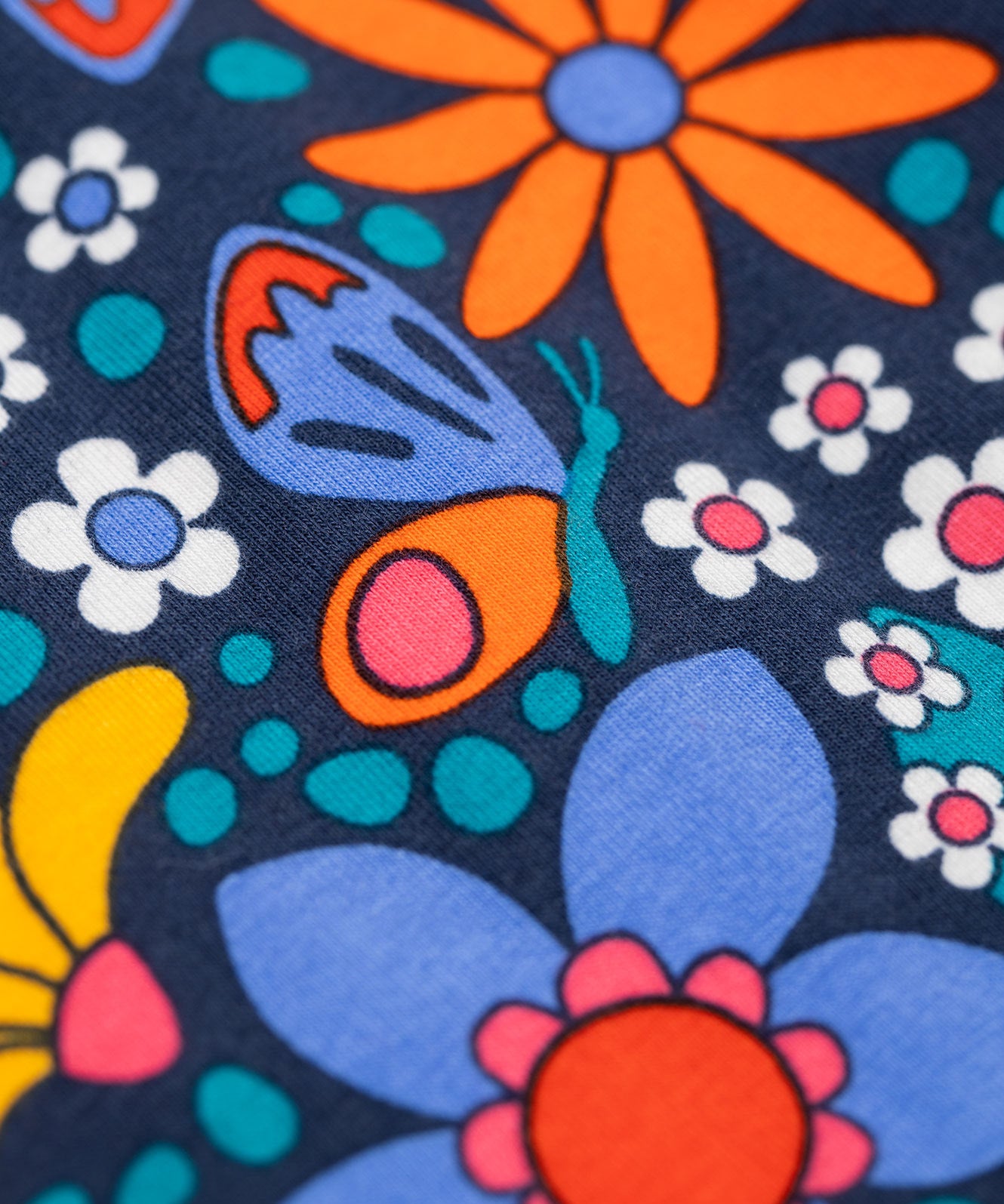 A close up of the details on the print of the Frugi sofia skater dress in navy / retro flowers available at Babipur. A GOTS organic cotton skater dress in navy with a bright retro floral design.