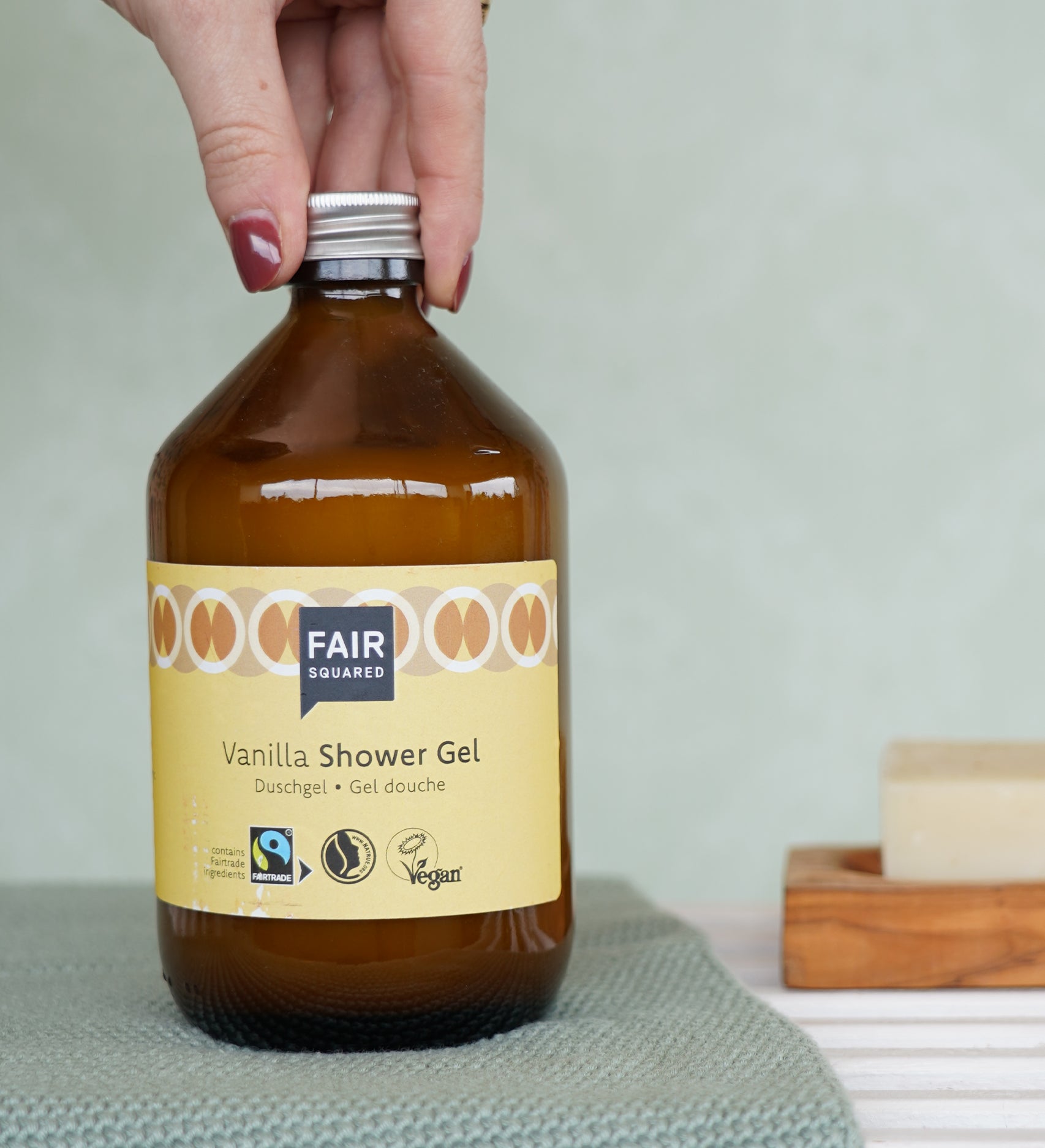 A glass bottle of Fair Squared Fairtrade Vanilla Shower Gel 500ml in a bathroom - vegan, cruelty free and plastic free - for sale at Babipur.