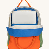 The organic cotton kids Fluf B-Pack Jr in cobalt orange, the backpack is unzipped and there's a small laptop inside.