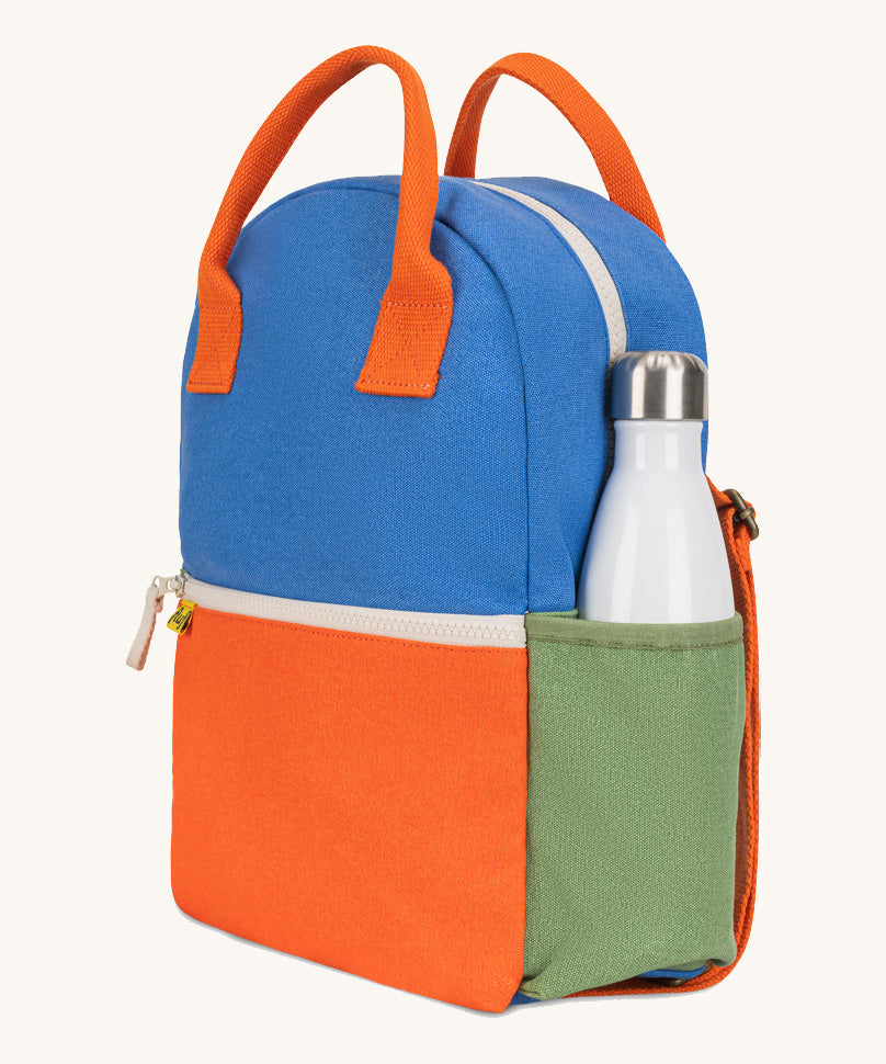 A side view of The organic cotton Fluf B-Pack Jr in cobalt orange, a kids school backpack with a green drink holder side pocket