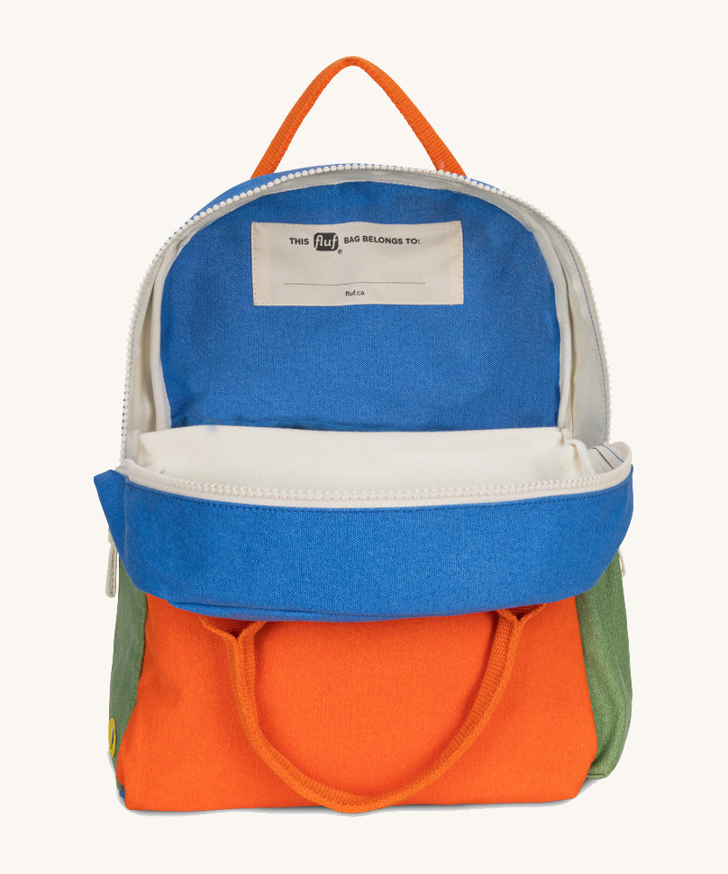 The organic cotton Fluf B-Pack Jr in cobalt orange, a kids school backpack, unzipped to show the name tag inside.