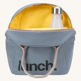 Fluf zip lunch bag in a light blue colour with a brown handle and a yellow inner lining holding a bottle on acream background.