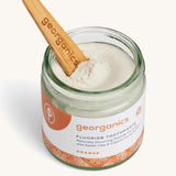 A opened jar of the orange fluoride toothpaste with the wooden spatula dipped in.