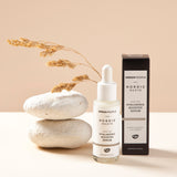 The Green People Nordic Roots Hyaluronic Booster Serum stood next to its box with white rocks just behind the bottle and dried grass