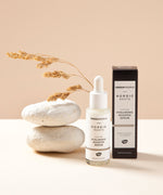 The Green People Nordic Roots Hyaluronic Booster Serum stood next to its box with white rocks just behind the bottle and dried grass