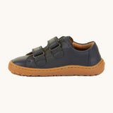 A side image of the Froddo barefoot base children's shoe in navy available at Babipur. A dark turquoise natural leather low profile shoe showing the 2 velcro fasteners looped through and the brown grippy sole