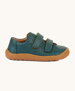 A side image of the Froddo barefoot base children's shoe in petroleum available at Babipur. A dark turquoise natural leather low profile shoe showing the 2 velcro fasteners and the brown grippy sole