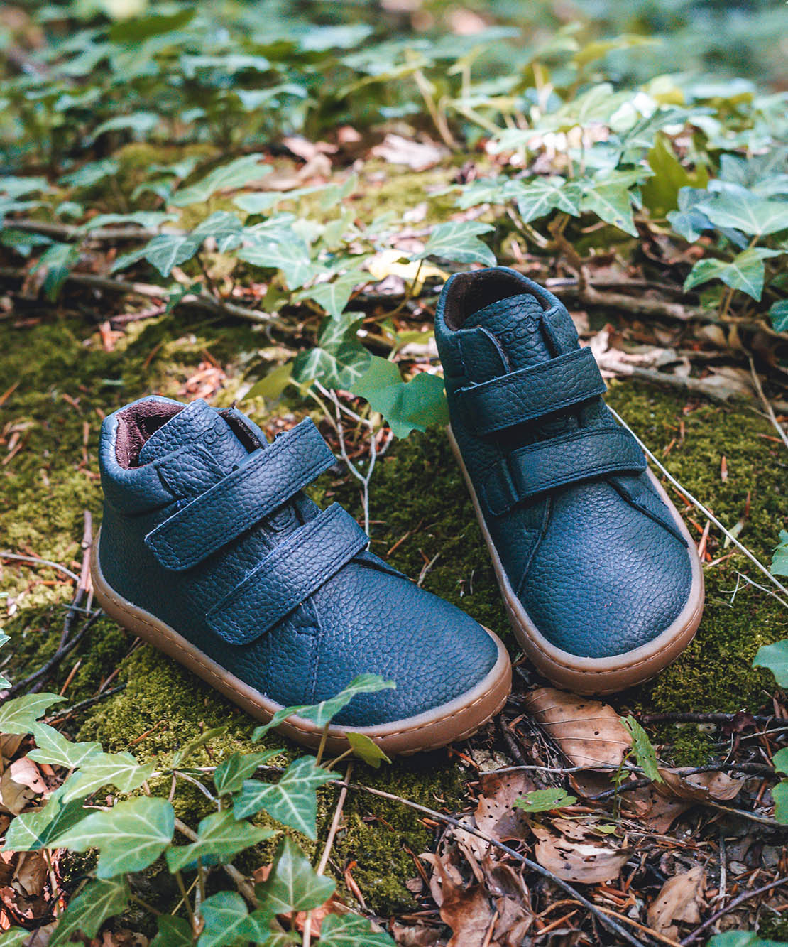 Froddo barefoot Autumn children's shoe in navy standing on a leaves. A natural leather shoe with a 2 velcro fastener for a secure fit, padded ankle and a dark brown grippy sole available at Babipur.