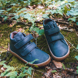 Froddo barefoot Autumn children's shoe in navy standing on a leaves. A natural leather shoe with a 2 velcro fastener for a secure fit, padded ankle and a dark brown grippy sole available at Babipur.
